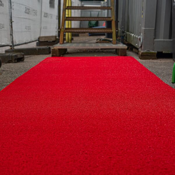 A Heavy-Duty PVC Vinyl Roll in bright red is laid out outdoors, leading up to metal steps surrounded by construction materials and containers.