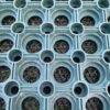 Close-up of the Green Grass Mat showing its textured green rubber surface with a grid of large circular holes, small corner circles, and a dark mesh-like layer beneath.
