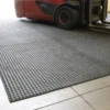 A red forklift drives over the Heavy-Duty Heavy Traffic Doorway Mat, a large, textured anti-fatigue mat on an industrial floor with visible tile lines.
