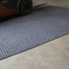 A forklift wheel rests on the Heavy-Duty Heavy Traffic Doorway Mat, a textured grey mat placed on a smooth concrete floor in an industrial or warehouse environment.