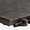 Close-up of the Interlocking Solid Top Gym Mat, showing its textured, rectangular surface with a rough pattern. A cylindrical knob is attached to the lower right corner. The background is plain and light-coloured.