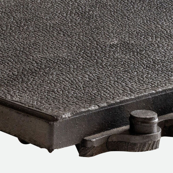 Close-up of the Interlocking Solid Top Gym Mat, showing its textured, rectangular surface with a rough pattern. A cylindrical knob is attached to the lower right corner. The background is plain and light-coloured.