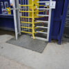 A yellow metal turnstile is bent at the entrance, allowing easy access. The area has blue walls and features a Grass Mat Roll (1m x 10m x 22mm) installed on the ground.