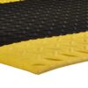 Close-up of the Comfort Plus Anti-Fatigue Mat shows a textured surface with alternating yellow and black sections and raised oval bumps in a regular pattern, ideal for enhanced safety and comfort.