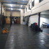 A dog lies on the floor of a spacious gym featuring Solid Top Gym Matting, with equipment along the walls and a person near boxing lockers and an exit door.