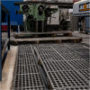 A factory floor features Interlocking Anti-Fatigue Mats alongside a large green industrial drilling machine, with pallets stacked below and various other workplace equipment visible.