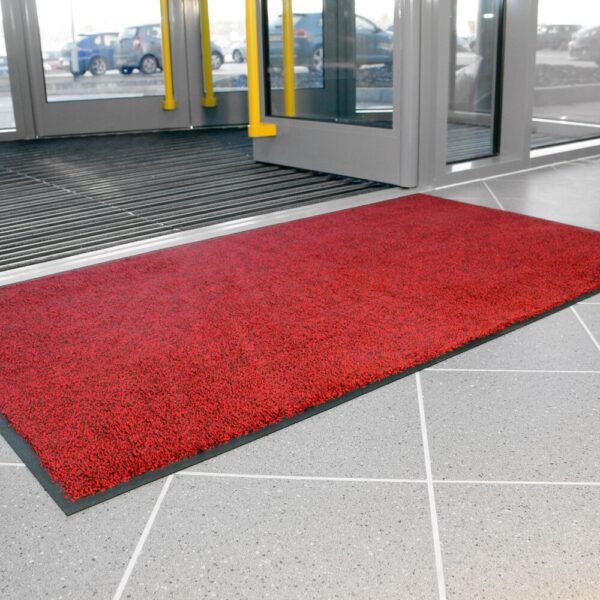 A High-Performance Entrance Mat in bright red is positioned just inside glass doors on light grey tiles, with cars visible outside.