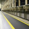 Rows of stacked tyres in an industrial warehouse, featuring a Standard Anti-Fatigue Mat with a yellow-striped walkway running alongside automated equipment and storage shelves.