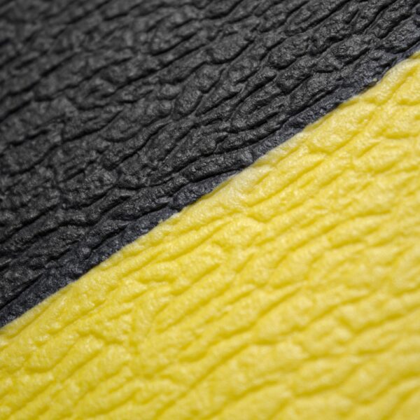Close-up of a Standard Anti-Fatigue Mat’s textured surface, divided diagonally with rough black on the upper left and similar yellow on the lower right, resembling synthetic rubber or plastic.