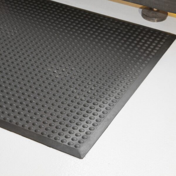 A close-up of the Air Cushioned Workshop Mat in black rubber, featuring a raised circular pattern, placed on a smooth, light-coloured floor.