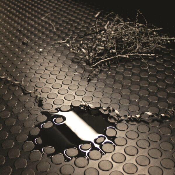 A puddle and dry twigs rest on Circular Stud Rubber Matting, whose textured black surface features circular patterns. Reflected light from the wet area contrasts with the matt background of the matting.