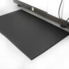 The Diamond Anti-Fatigue Mat, featuring a black diamond plate texture, is positioned on a white floor in front of a large industrial machine.