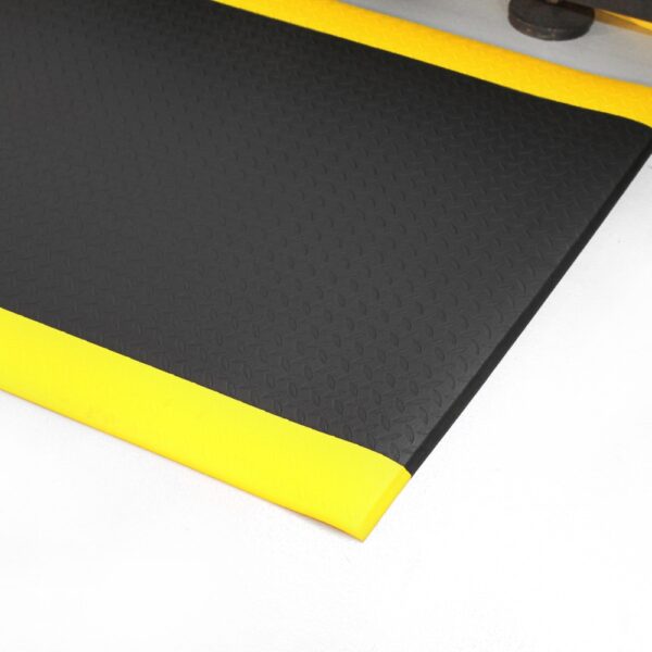 A close-up of the Diamond Anti-Fatigue Mat in black, featuring a textured surface and bright yellow bevelled edges, placed on a white floor.