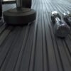 Three dumbbells sit on a Heavy-Duty Gym Mat’s ribbed black surface, with two chrome dumbbells on the right and a larger matte black one on the left, all viewed from a low angle.