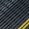 Close-up of the Self-Draining Safety Mat featuring black textured parallel slats arranged diagonally, with one yellow and green slat adding a bold contrast.