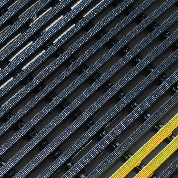Close-up of the Self-Draining Safety Mat featuring black textured parallel slats arranged diagonally, with one yellow and green slat adding a bold contrast.