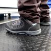 A person stands on a Comfort Plus Anti-Fatigue Mat with a black diamond plate texture, wearing black work shoes and dark trousers, likely in an industrial or workshop setting.