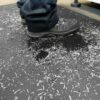 Close-up of a person wearing black work shoes standing on the Ultimate Anti-Fatigue Mat, which is covered with metal or plastic shavings in an industrial setting.