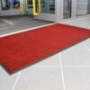 A red Ribbed Doormat is placed on a light grey tiled floor in front of partially open glass doors, featuring a visible yellow handle.