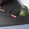 A welding helmet and a welding torch with a black cable rest on a Diamond Welding Mat, which is placed on a blue floor.