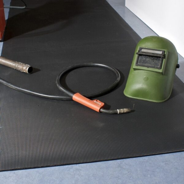 A welding helmet and a welding torch with a black cable rest on a Diamond Welding Mat, which is placed on a blue floor.