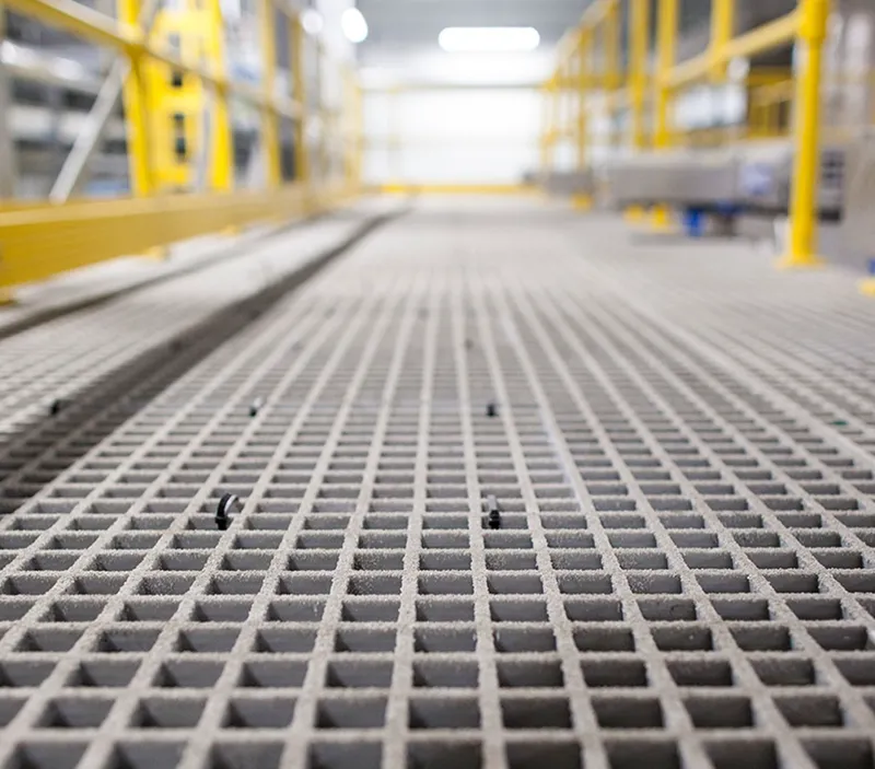Low-angle view of a metal grating walkway in an industrial setting, with yellow railings on the sides and shelves visible in the blurred background.