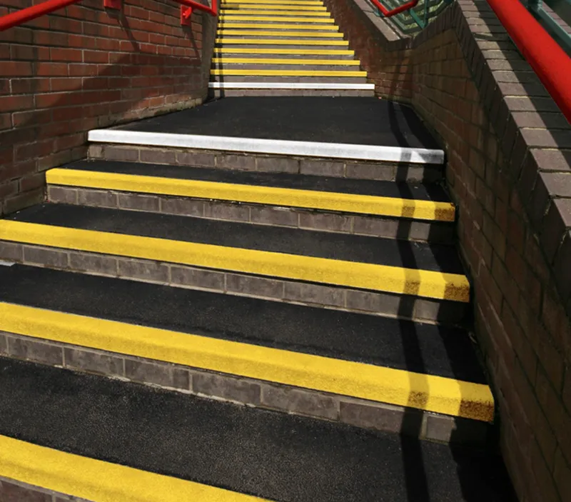 Concrete stairs bordered by brick walls and red railings, with each step marked by a bright yellow strip. One step near the centre has a single white strip instead of yellow.
