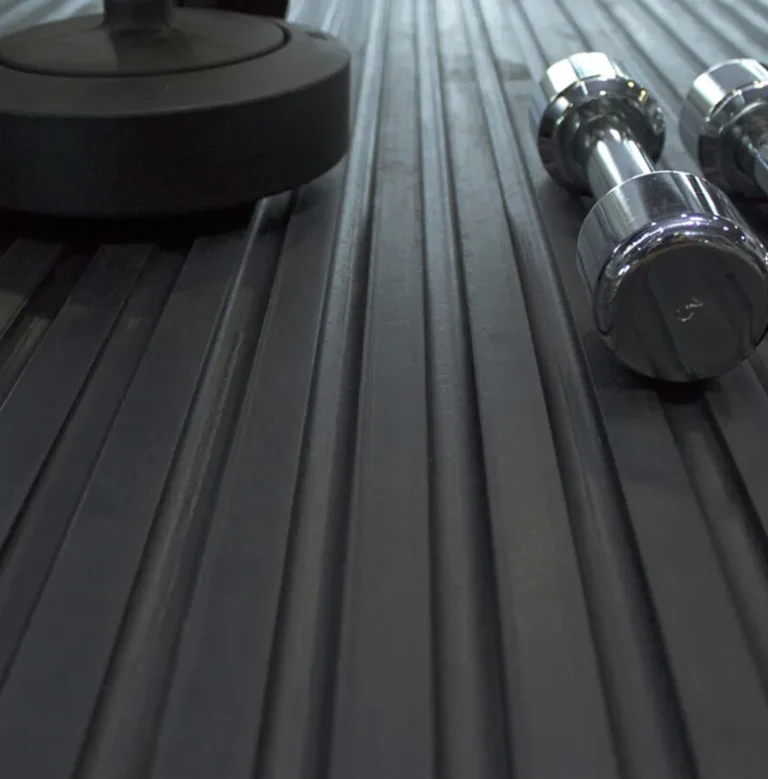 Close-up of a black ribbed gym floor mat with two chrome dumb-bells and the base of a larger weight resting on it.