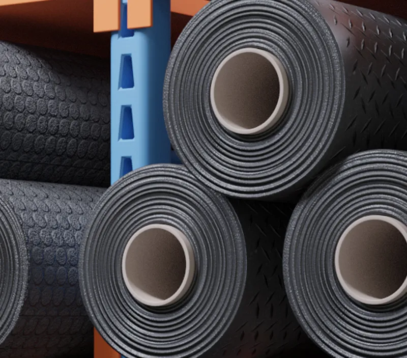 Large black rubber floor mats rolled up and stacked horizontally on a storage rack, with a blue metal support frame and textured surface patterns visible on the mats.